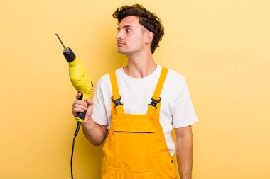 Profil görünümlü genç adam hayal mi kuruyor yoksa hayal mi kuruyor? Matkap konsepti olan bir tamirci.