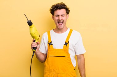 Genç yakışıklı adam agresif bir şekilde bağırıyor, çok kızgın görünüyor. Matkap konsepti olan bir tamirci.