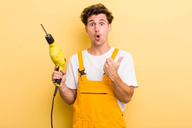 Genç ve yakışıklı bir adam inançsızlığa şaşırmış görünüyor. Matkap konsepti olan bir tamirci.