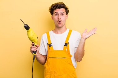 Genç, yakışıklı adam şaşırmış ve şok olmuş görünüyor. Çenesi düşmüş, elinde bir nesne var. Matkap konsepti olan bir tamirci.