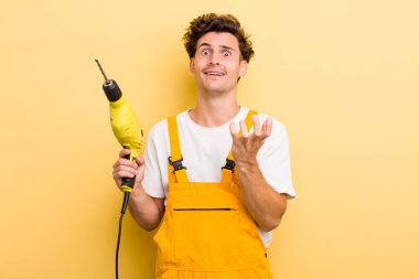 Genç ve yakışıklı adam umutsuz, sinirli ve stresli görünüyor. Matkap konsepti olan bir tamirci.