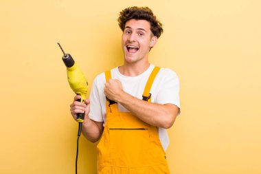 Genç yakışıklı adam kendini mutlu hissediyor ve bir meydan okumayla yüzleşiyor ya da kutluyor. Matkap konsepti olan bir tamirci.