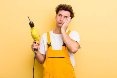 Genç ve yakışıklı bir adam bıkkın, yorgun ve uykulu hissediyor. Matkap konsepti olan bir tamirci.