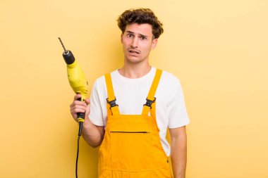 Genç yakışıklı adam şaşkın ve şaşkın hissediyor. Matkap konsepti olan bir tamirci.