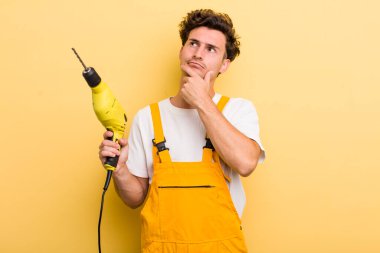 Genç yakışıklı adam düşünüyor, kuşkulu ve şaşkın hissediyor. Matkap konsepti olan bir tamirci.