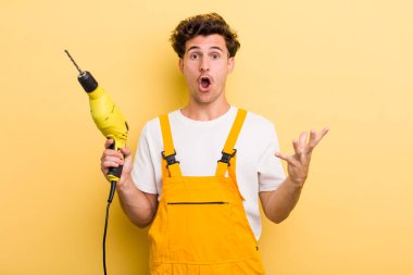 Genç ve yakışıklı adam şok olmuş ve şaşırmış hissediyor. Matkap konsepti olan bir tamirci.
