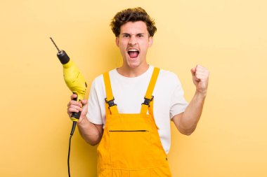 Genç yakışıklı adam sinirli bir ifadeyle agresif bir şekilde bağırıyor. Matkap konsepti olan bir tamirci.