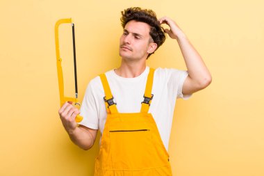 Genç yakışıklı adam mutlu bir şekilde gülümsüyor ve hayal kuruyor ya da şüphe ediyor. Tamirci ve testere konsepti