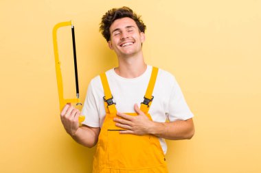 Genç yakışıklı adam komik bir şakaya yüksek sesle gülüyor. Tamirci ve testere konsepti