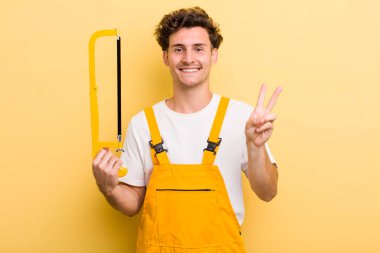 Genç yakışıklı adam gülümsüyor ve mutlu görünüyor, zafer ya da barış işareti yapıyor. Tamirci ve testere konsepti