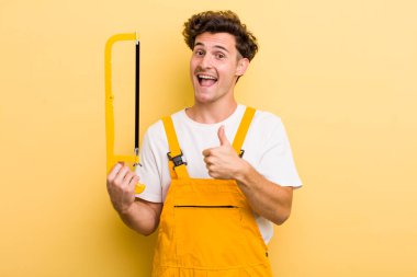 Genç yakışıklı adam gururlu, olumlu gülümsüyor. Tamirci ve testere konsepti