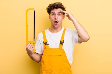 Genç yakışıklı adam mutlu, şaşkın ve şaşırmış görünüyor. Tamirci ve testere konsepti
