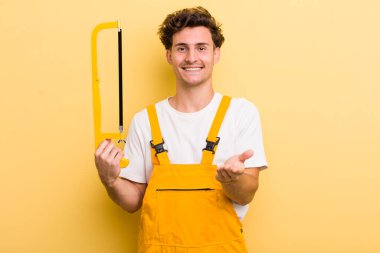 Genç yakışıklı adam mutlu bir şekilde gülümsüyor ve bir konsept sunuyor. Tamirci ve testere konsepti