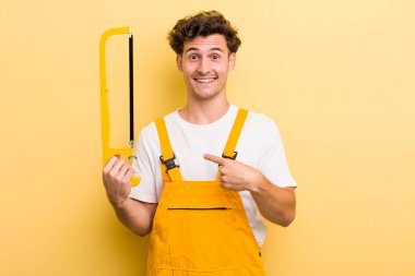 Genç yakışıklı adam kendini mutlu hissediyor ve heyecanla kendini işaret ediyor. Tamirci ve testere konsepti