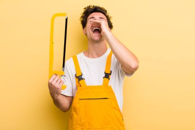 Genç yakışıklı adam kendini mutlu hissediyor, elleri ağzının kenarında bağırıyor. Tamirci ve testere konsepti