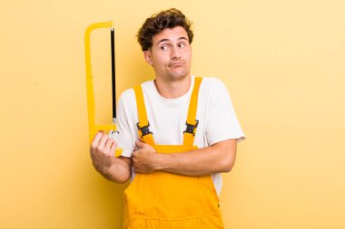 Genç yakışıklı adam omuz silkiyor, kafası karışık ve kararsız hissediyor. Tamirci ve testere konsepti