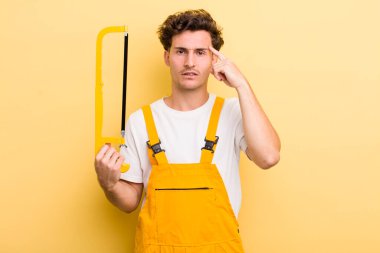 Genç yakışıklı, kafası karışık ve şaşkın hissediyor, sana deli olduğunu gösteriyor. Tamirci ve testere konsepti