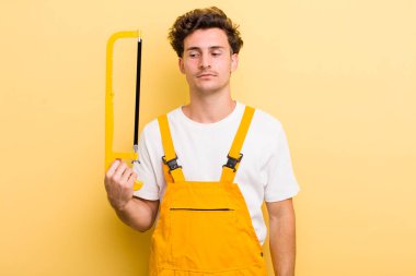 Genç yakışıklı adam üzgün, üzgün ya da kızgın hissediyor ve yana bakıyor. Tamirci ve testere konsepti