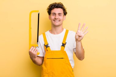 Genç yakışıklı adam gülümsüyor ve arkadaş canlısı görünüyor, dört numarayı gösteriyor. Tamirci ve testere konsepti
