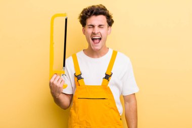 Genç yakışıklı adam agresif bir şekilde bağırıyor, çok kızgın görünüyor. Tamirci ve testere konsepti