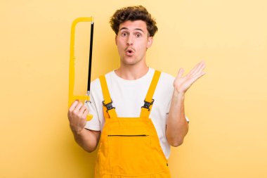 Genç, yakışıklı adam şaşırmış ve şok olmuş görünüyor. Çenesi düşmüş, elinde bir nesne var. Tamirci ve testere konsepti