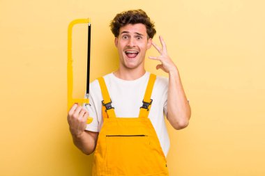 Genç yakışıklı adam ellerini havaya kaldırarak çığlık atıyor. Tamirci ve testere konsepti