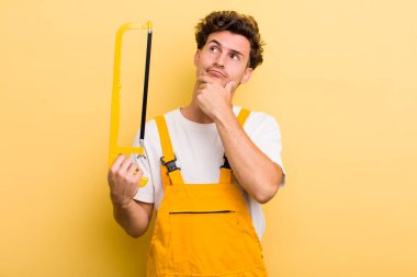 Genç yakışıklı adam düşünüyor, kuşkulu ve şaşkın hissediyor. Tamirci ve testere konsepti