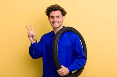 Genç yakışıklı adam gülümsüyor ve mutlu görünüyor, zafer ya da barış işareti yapıyor. motor mekaniği kavramı