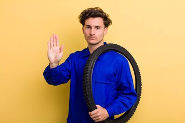 Genç ve yakışıklı adam ciddi görünüyor. Avuç içi gösteriyor. Durma hareketi yapıyor. motor mekaniği kavramı