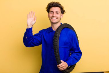 Genç yakışıklı adam mutlu bir şekilde gülümsüyor, el sallıyor, hoş geldin diyor ve seni selamlıyor. motor mekaniği kavramı