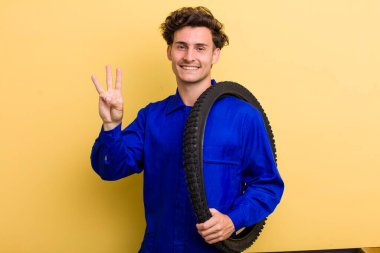 Genç yakışıklı adam gülümsüyor ve arkadaş canlısı görünüyor, üç numarayı gösteriyor. motor mekaniği kavramı
