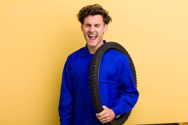 Genç yakışıklı adam agresif bir şekilde bağırıyor, çok kızgın görünüyor. motor mekaniği kavramı