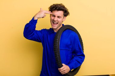 Genç yakışıklı adam mutsuz ve stresli görünüyor, intihar jesti silah işareti yapıyor. motor mekaniği kavramı