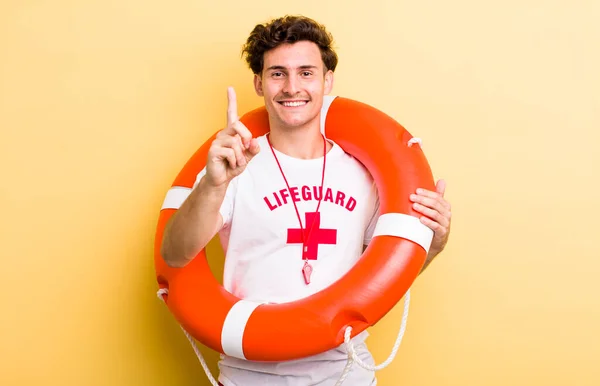 young handsome guy smiling proudly and confidently making number one. lifeguard concept