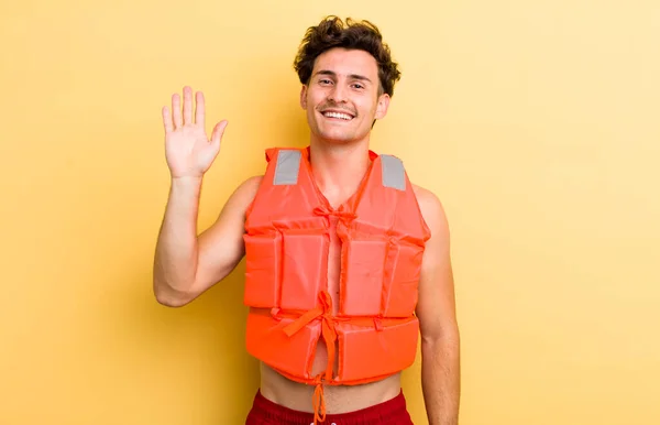 笑顔で手を振って歓迎し挨拶する若いハンサムな男 ライフジャケットとボートのコンセプト — ストック写真