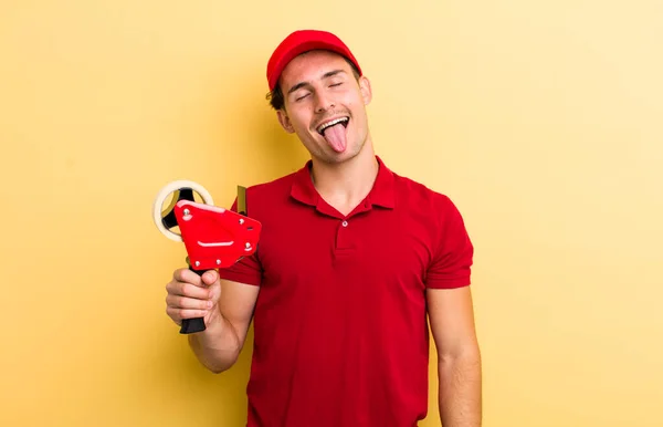 陽気で反抗的な態度を持つ若いハンサムな男冗談と舌を突き出す パッカー社員のコンセプト — ストック写真