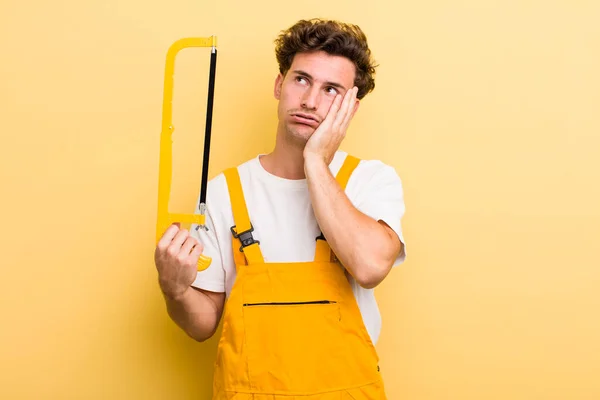 young handsome guy feeling bored, frustrated and sleepy after a tiresome. handyman and a saw concept