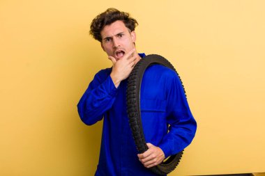 Ağzı ve gözleri sonuna kadar açık ve eli çenesinde olan yakışıklı bir genç. motor mekaniği kavramı