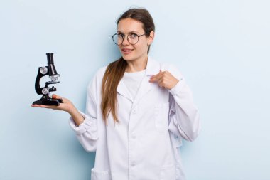 Genç yetişkin bir kadın kendini mutlu hissediyor ve heyecanlı bir şekilde kendini işaret ediyor. Mikroskoplu bir bilim adamı
