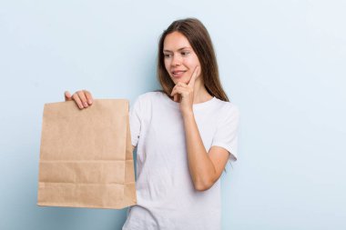 Genç yetişkin bir kadın mutlu ve kendinden emin bir ifadeyle gülümsüyor, elleri çenesinde. teslimat ve paket konsepti