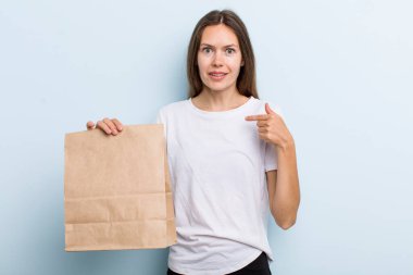 Genç yetişkin bir kadın kendini mutlu hissediyor ve heyecanlı bir şekilde kendini işaret ediyor. teslimat ve paket konsepti