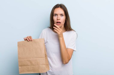 Ağzı ve gözleri açık ve eli çenesinde olan genç bir kadın. teslimat ve paket konsepti