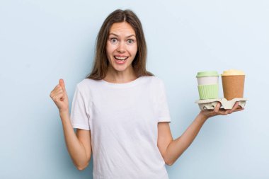 Genç bir kadın şokta, gülüyor ve başarıyı kutluyor. kahve konseptini kaldır.