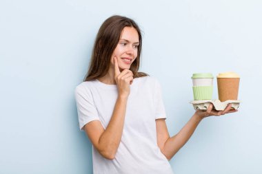 Genç yetişkin bir kadın mutlu ve kendinden emin bir ifadeyle gülümsüyor, elleri çenesinde. kahve konseptini kaldır.