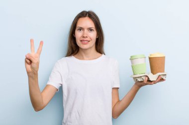 Genç yetişkin kadın gülümsüyor ve arkadaş canlısı görünüyor, iki numarayı gösteriyor. kahve konseptini kaldır.