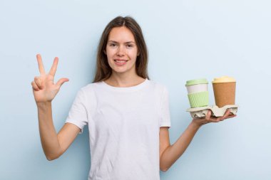 Genç yetişkin kadın gülümsüyor ve arkadaş canlısı görünüyor, üç numarayı gösteriyor. kahve konseptini kaldır.