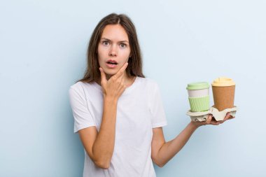 Ağzı ve gözleri açık ve eli çenesinde olan genç bir kadın. kahve konseptini kaldır.