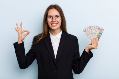 Genç yetişkin bir kadın kendini mutlu hissediyor. Onayını iyi bir jestle gösteriyor. Dolar banknotları konsepti
