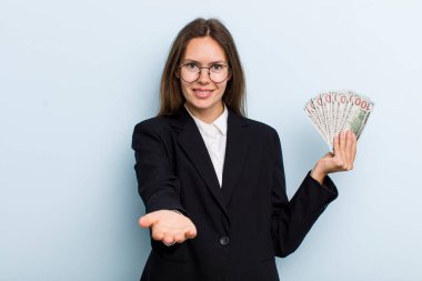 Genç yetişkin bir kadın arkadaşça gülümsüyor ve bir konsept sunuyor. Dolar banknotları konsepti