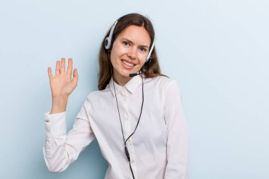 young adult woman smiling happily, waving hand, welcoming and greeting you. telemarketer concept